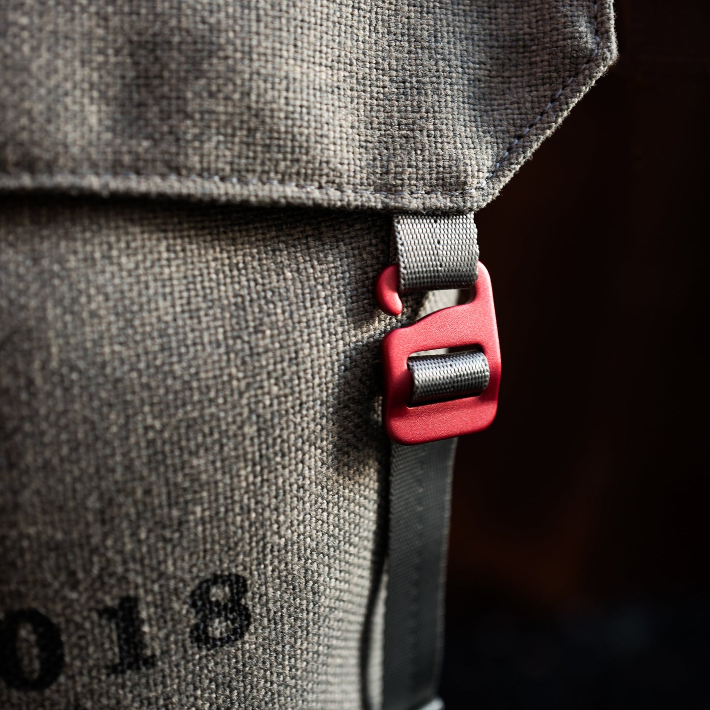 Close-up of red anodized aluminum clip on a Fierce Hazel convertible small messenger bag made with sustainable fabric. Functional, rugged and water-resistant it is military styled but beautiful